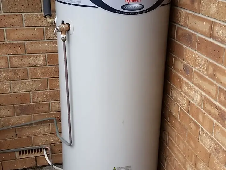 Storage hot water tank replaced against a brick wall with new tempering valve